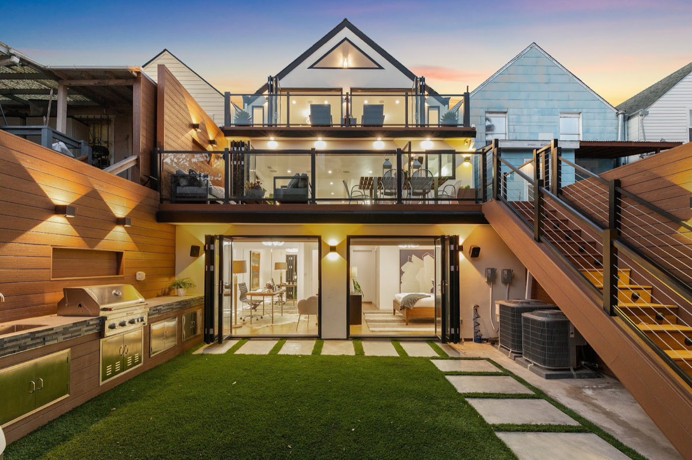 Modern custom home at dusk with tiered deck and glass railings